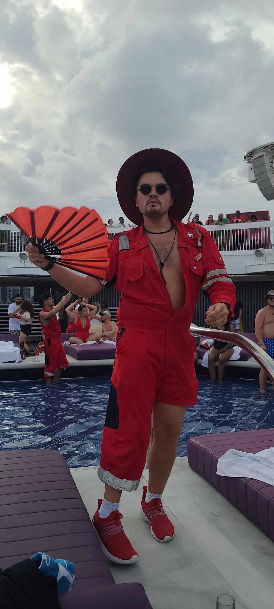 A performer in a red jumpsuit and wide-brimmed hat holding a red folding fan on the pool deck