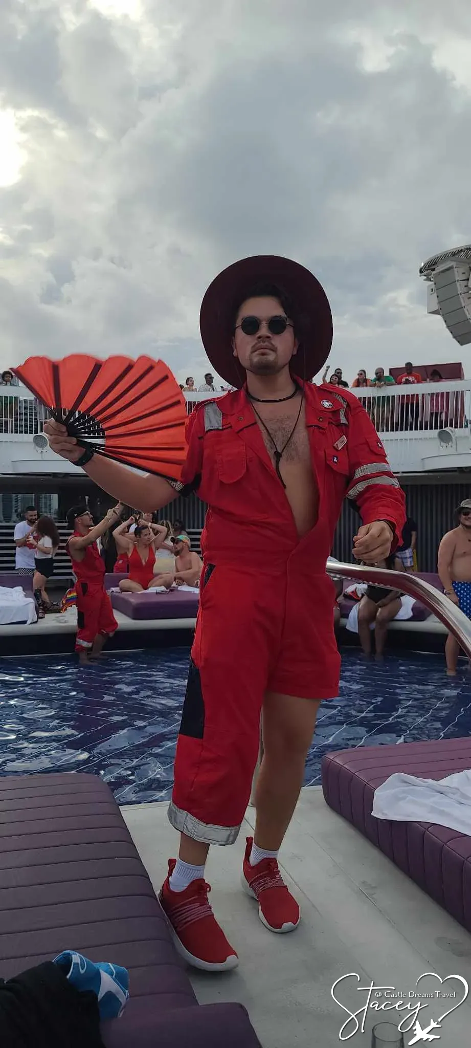 A performer in a red jumpsuit and wide-brimmed hat holding a red folding fan on the pool deck