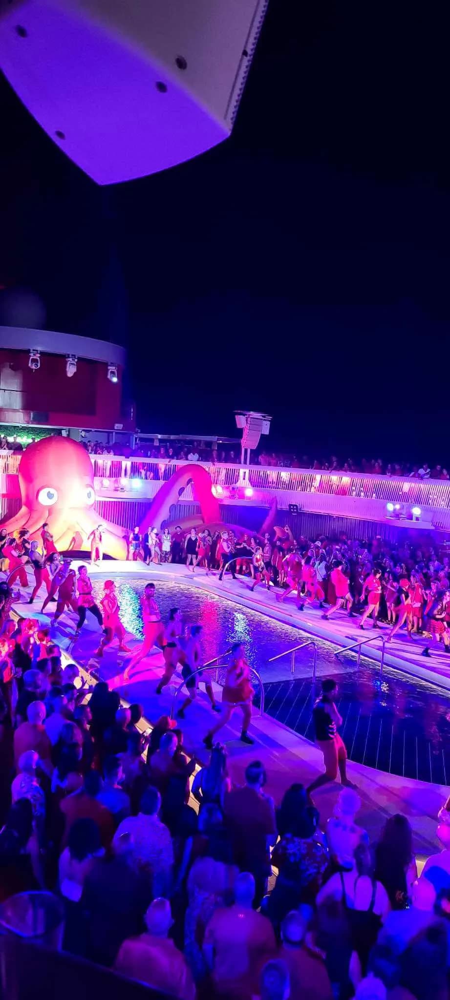 Nighttime pool-deck party on a Virgin Voyages ship with performers, crowds, and a giant inflatable octopus