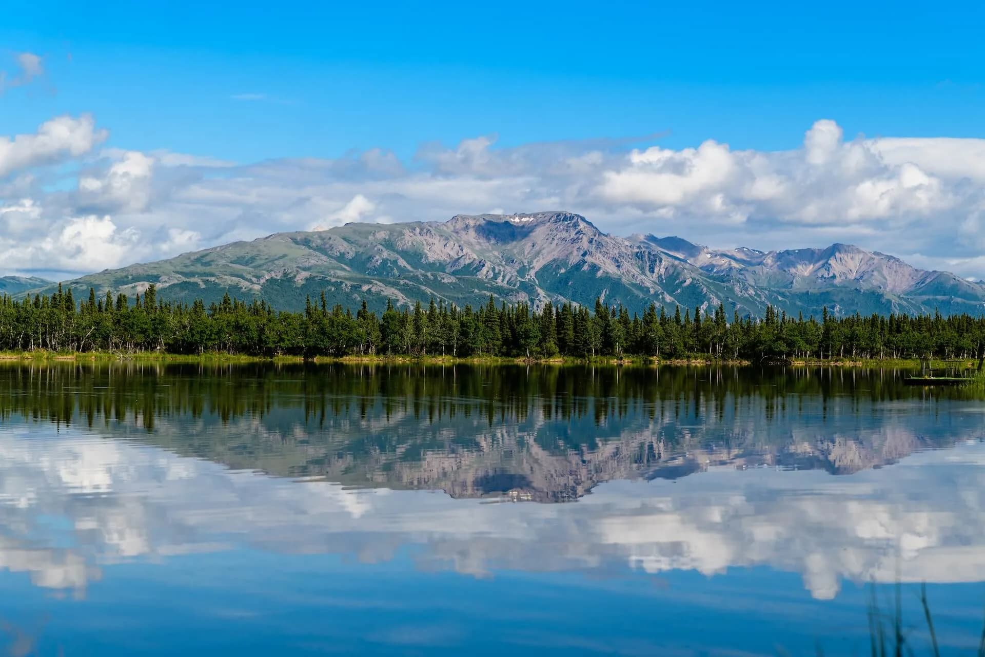 Snow-patched mountains and an evergreen shoreline reflected in a glassy Alaskan lake