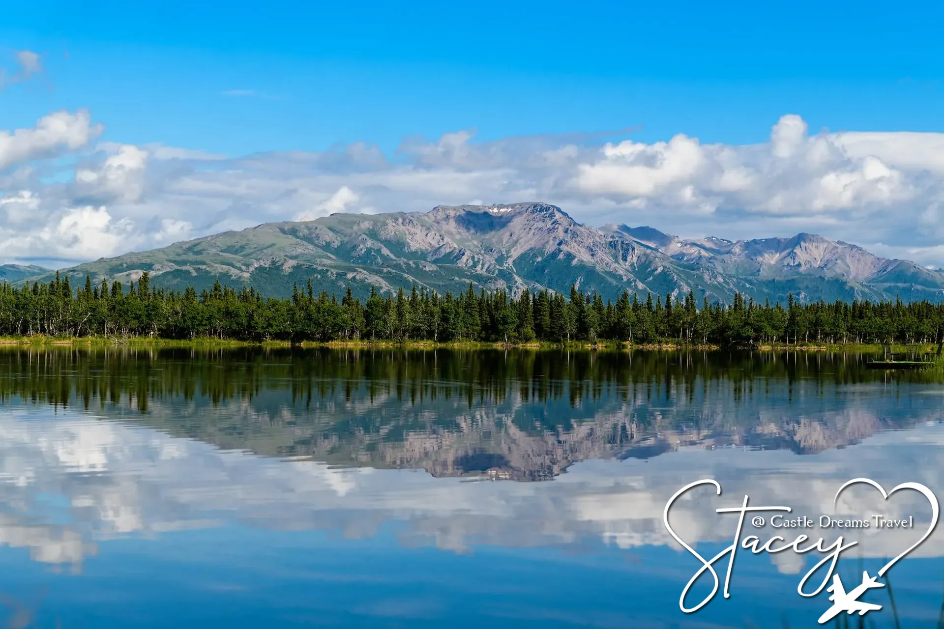 Snow-patched mountains and an evergreen shoreline reflected in a glassy Alaskan lake