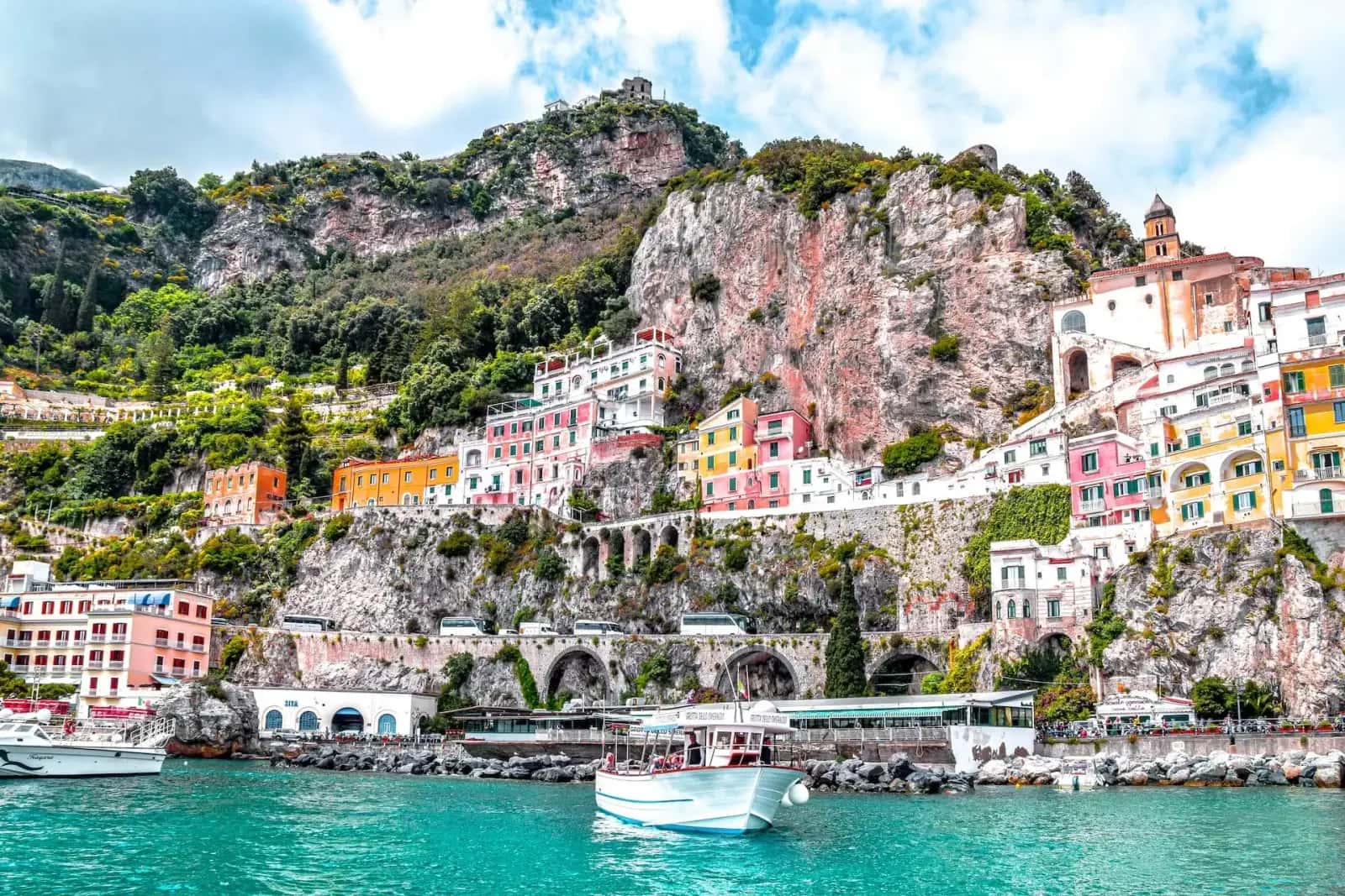 Boats on turquoise water beneath the colorful cliffside town of Amalfi, Italy