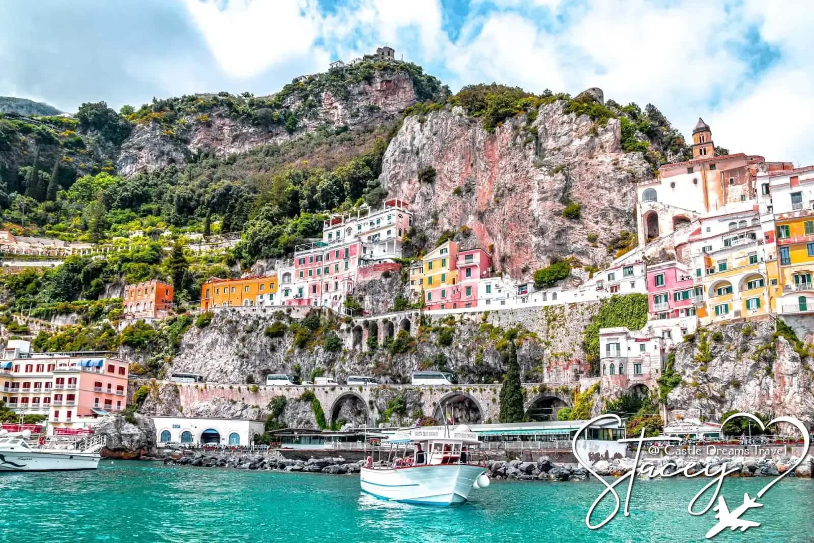 Boats on turquoise water beneath the colorful cliffside town of Amalfi, Italy