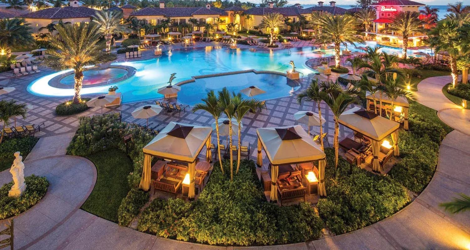 Pool, palm trees, and lit cabanas at dusk at a Beaches all-inclusive resort