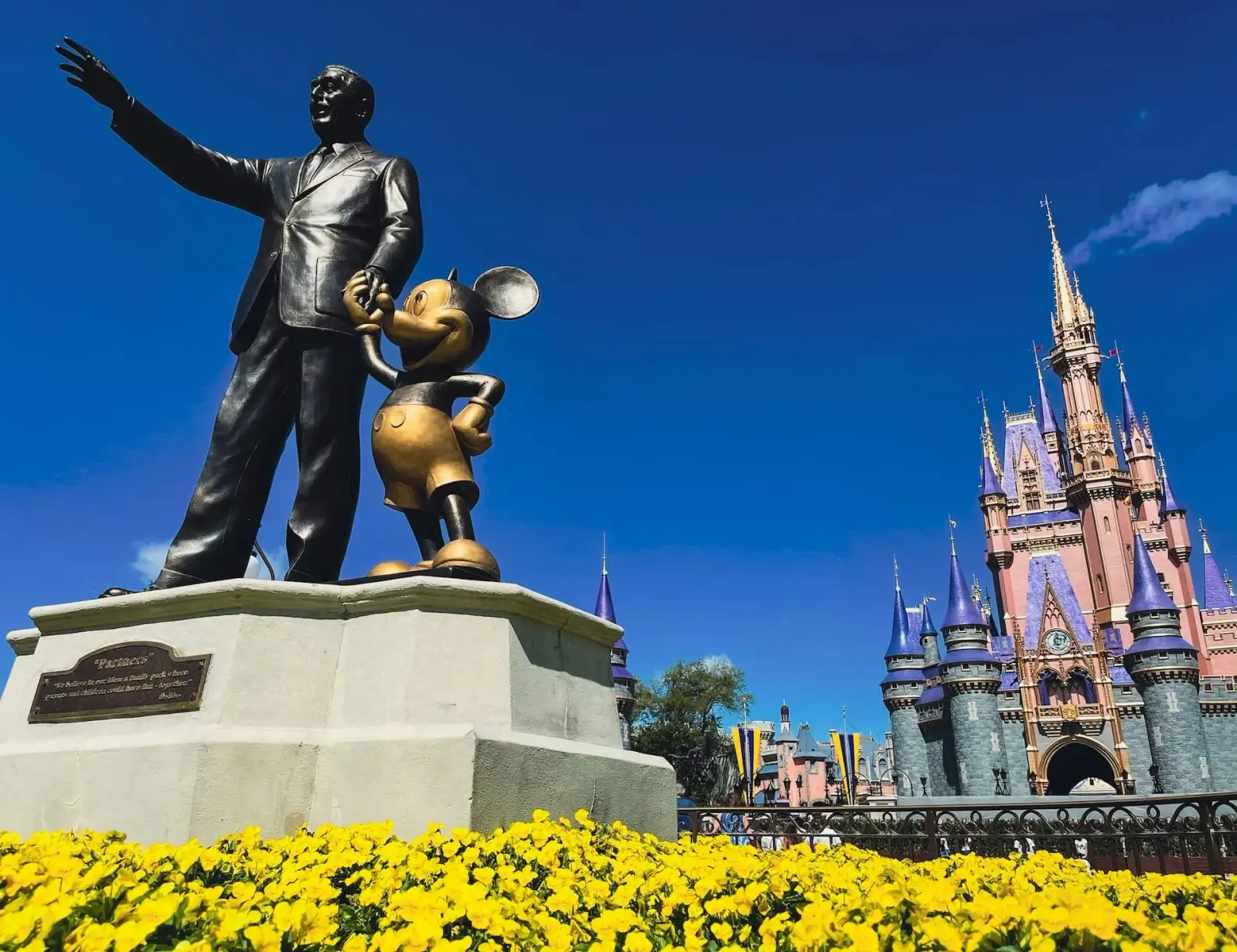 Partners statue of Walt Disney and Mickey Mouse in front of Cinderella Castle, with yellow flowers in bloom