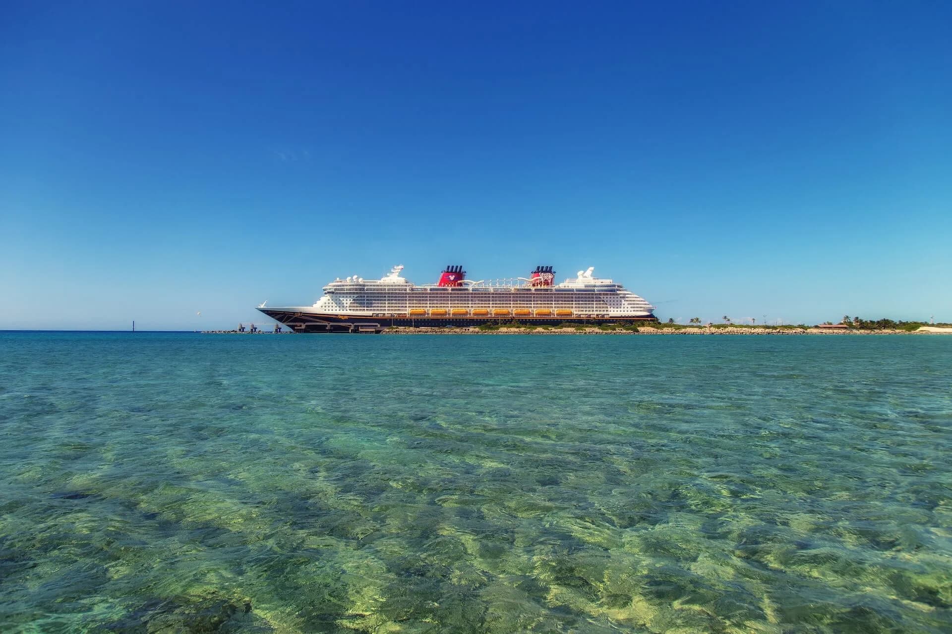 Disney Cruise Line ship at anchor off a white-sand island beach