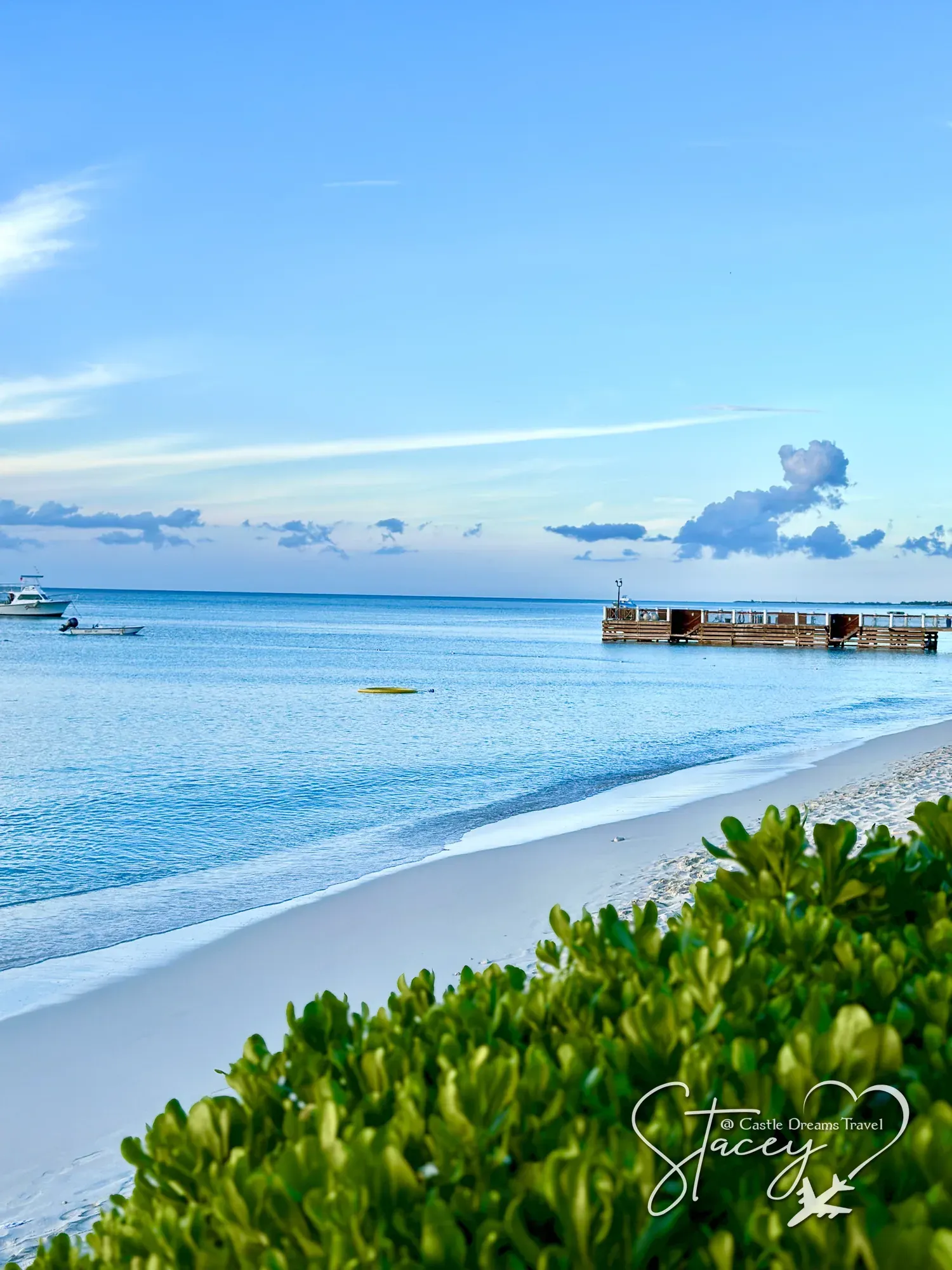 Clear turquoise water meeting white sand along Grace Bay, with a pier in the distance