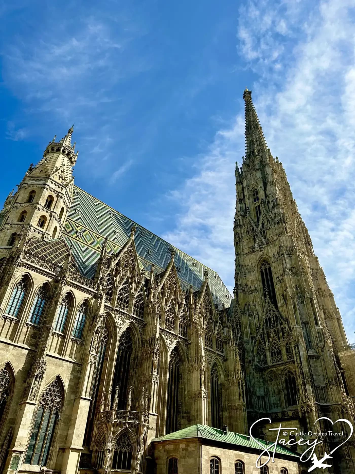 The gothic spire and patterned tile roof of St. Stephen's Cathedral in Vienna against a blue sky