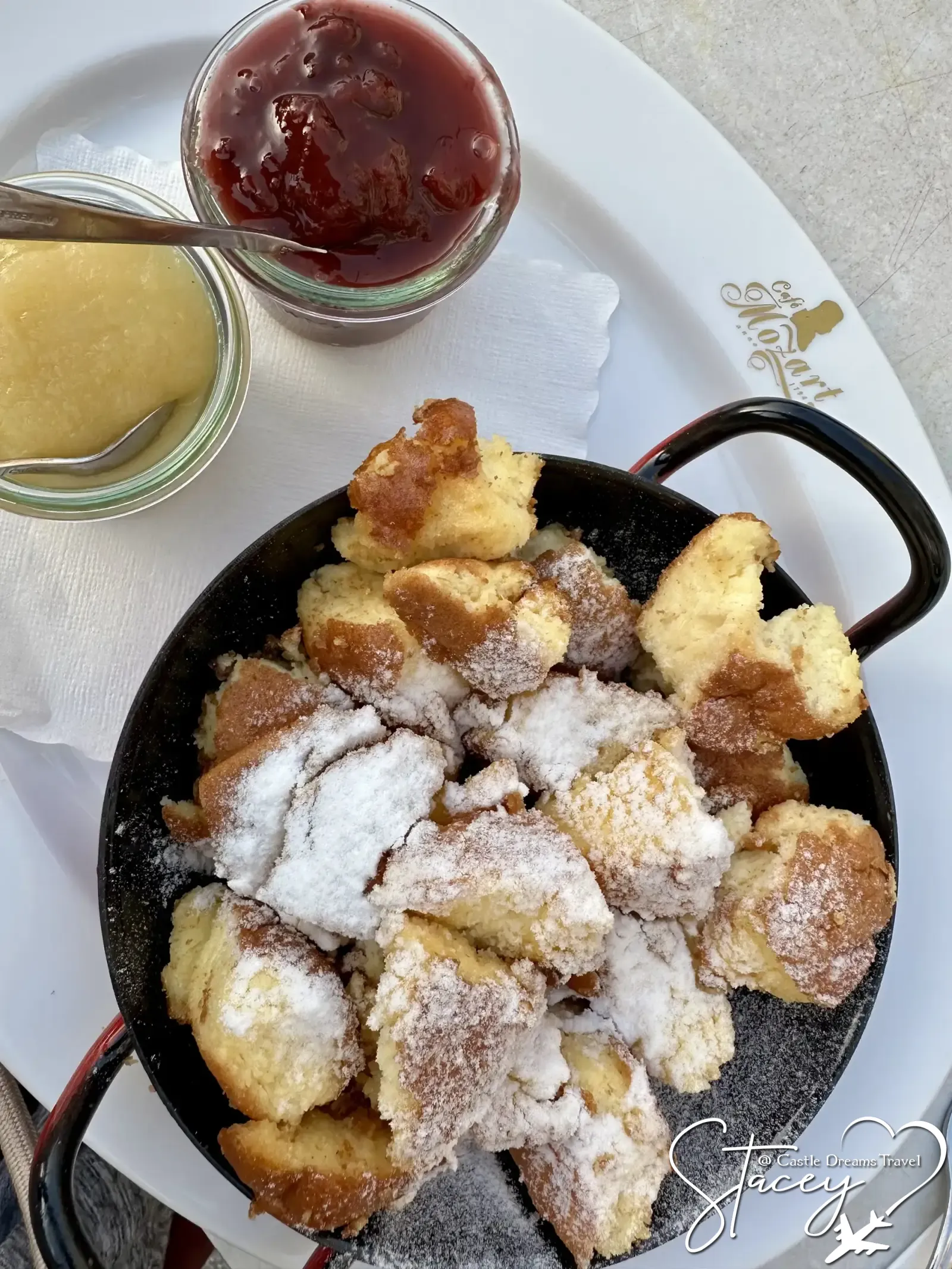 A cast-iron skillet of Kaiserschmarrn dusted with powdered sugar, served with fruit compote