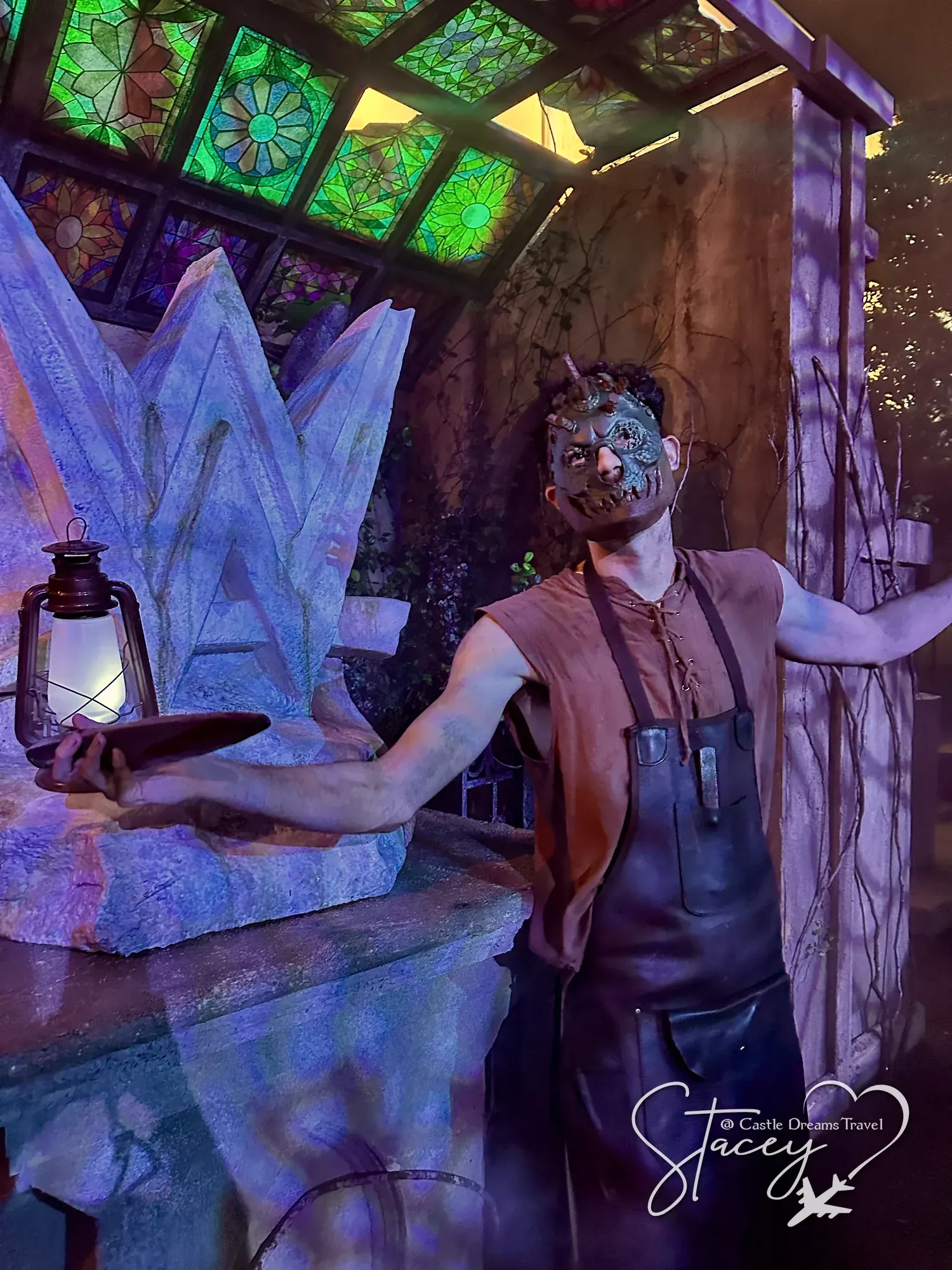 A Halloween Horror Nights scare actor in facial prosthetics holding a lantern beside a glowing ice-crystal set