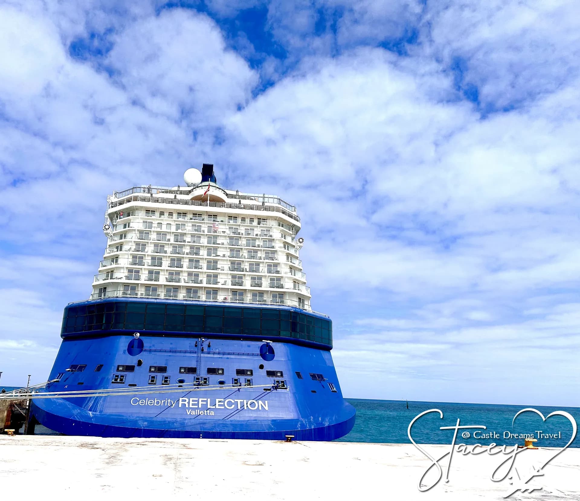 Celebrity Reflection docked under a bright cloud-streaked sky, her name along the dark blue hull
