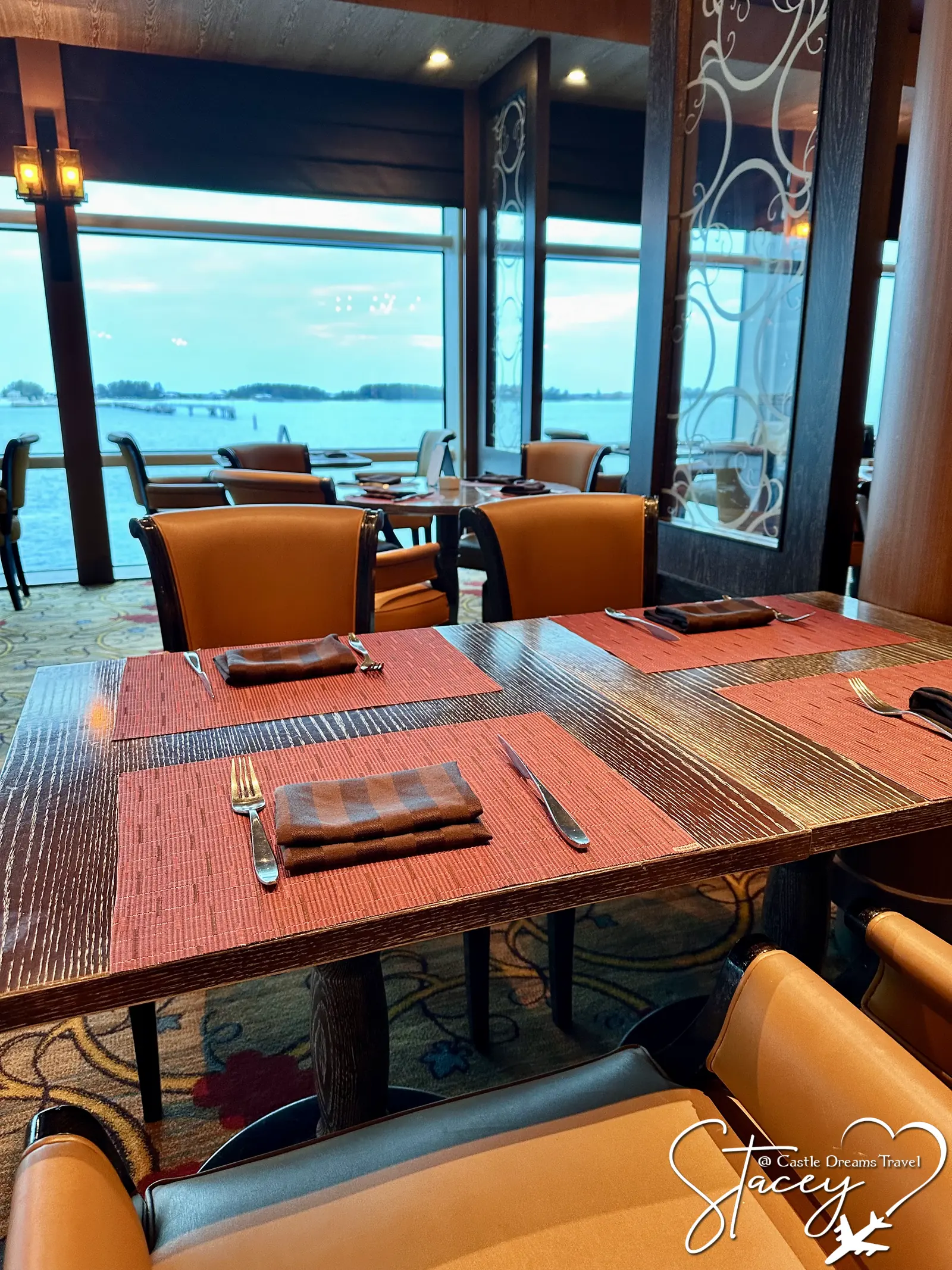 A set table in a Celebrity Cruises dining venue, floor-to-ceiling windows looking out over the water