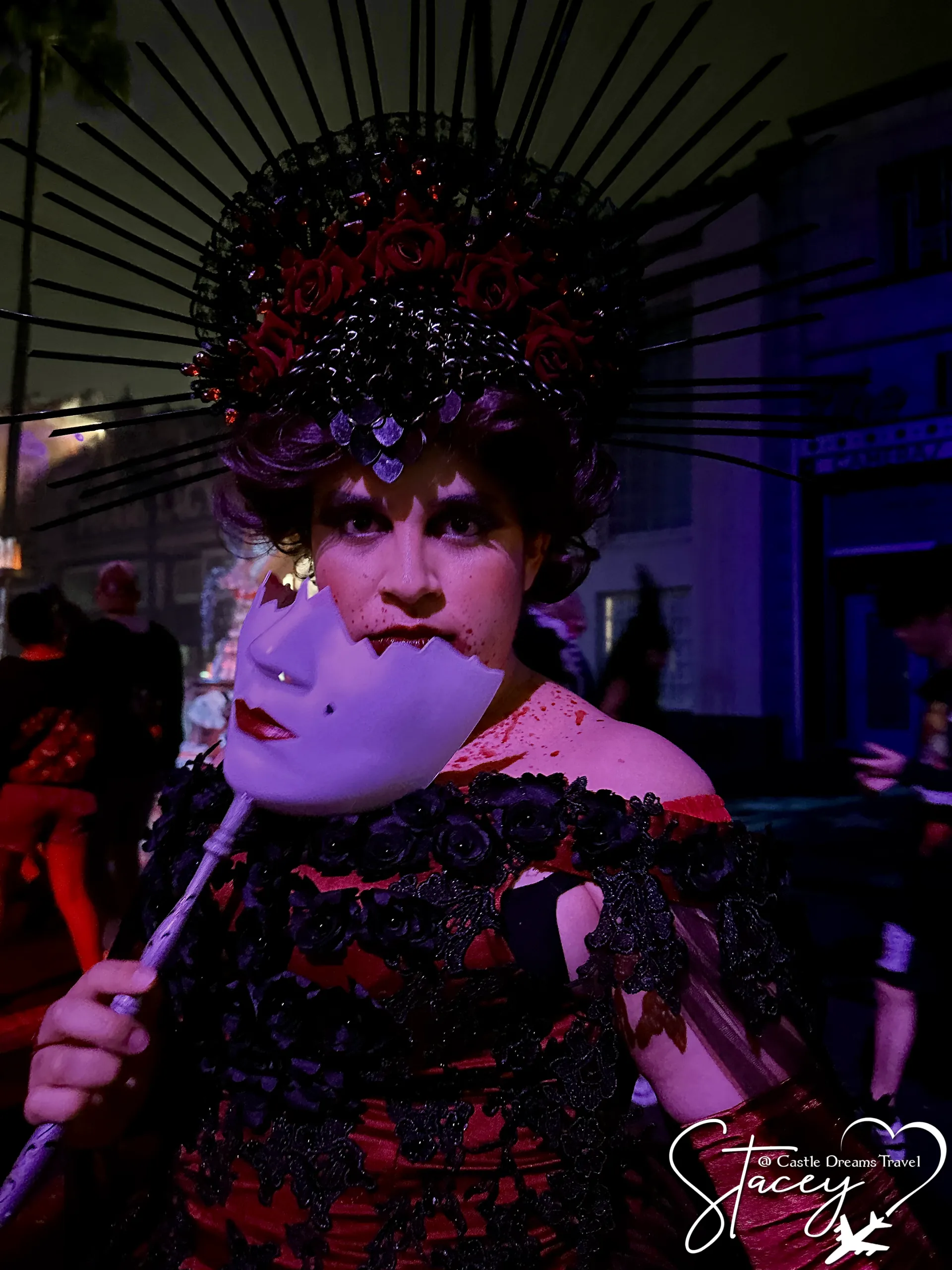 A performer in an elaborate beaded black headdress and gown holding a feathered fan
