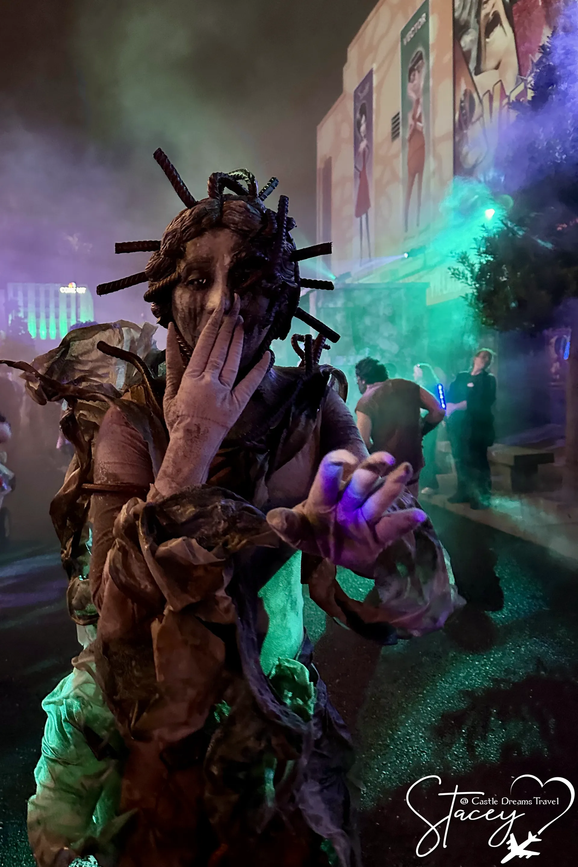 A scarecrow-costumed performer reaching forward through green fog in a Halloween Horror Nights scare zone