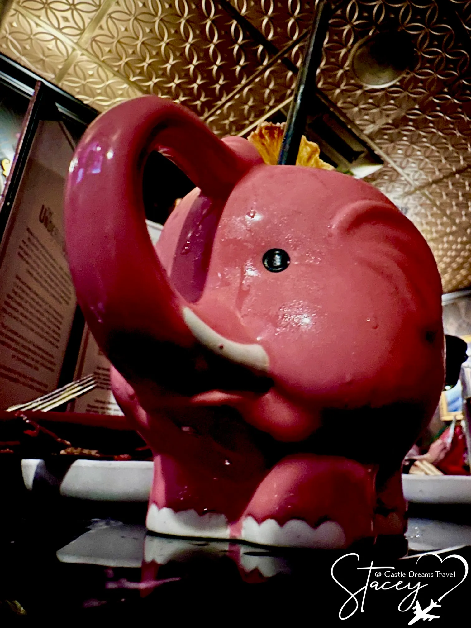 A cocktail served in a pink ceramic elephant mug on a patterned table