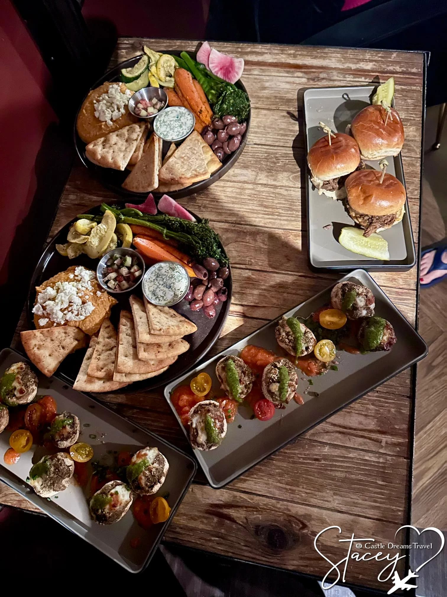 A wooden table covered with shared plates — charcuterie boards, sliders and appetizers