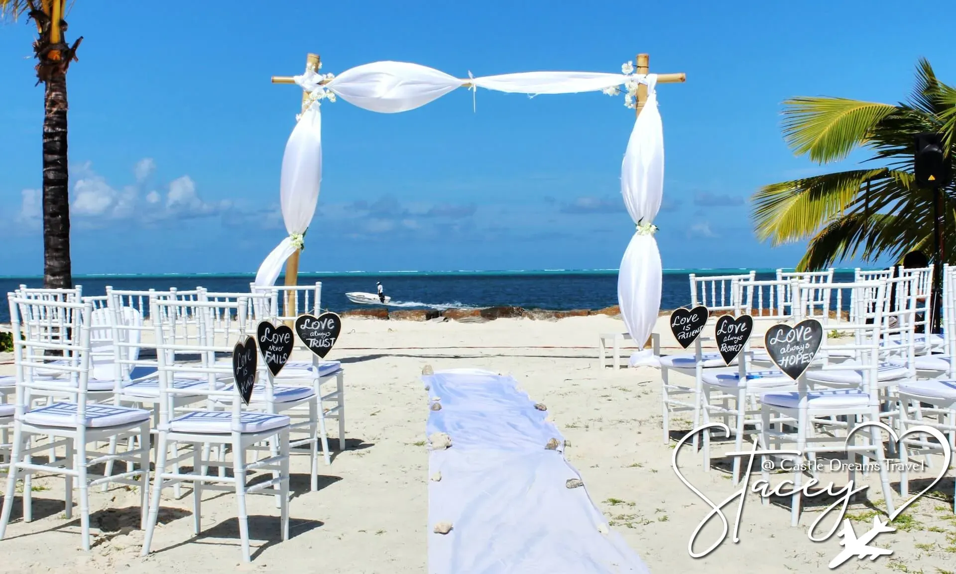 Rows of white chairs and a draped wedding arch set up for a beach ceremony