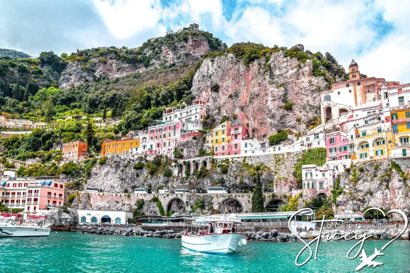 Boats on turquoise water beneath the colorful cliffside town of Amalfi, Italy