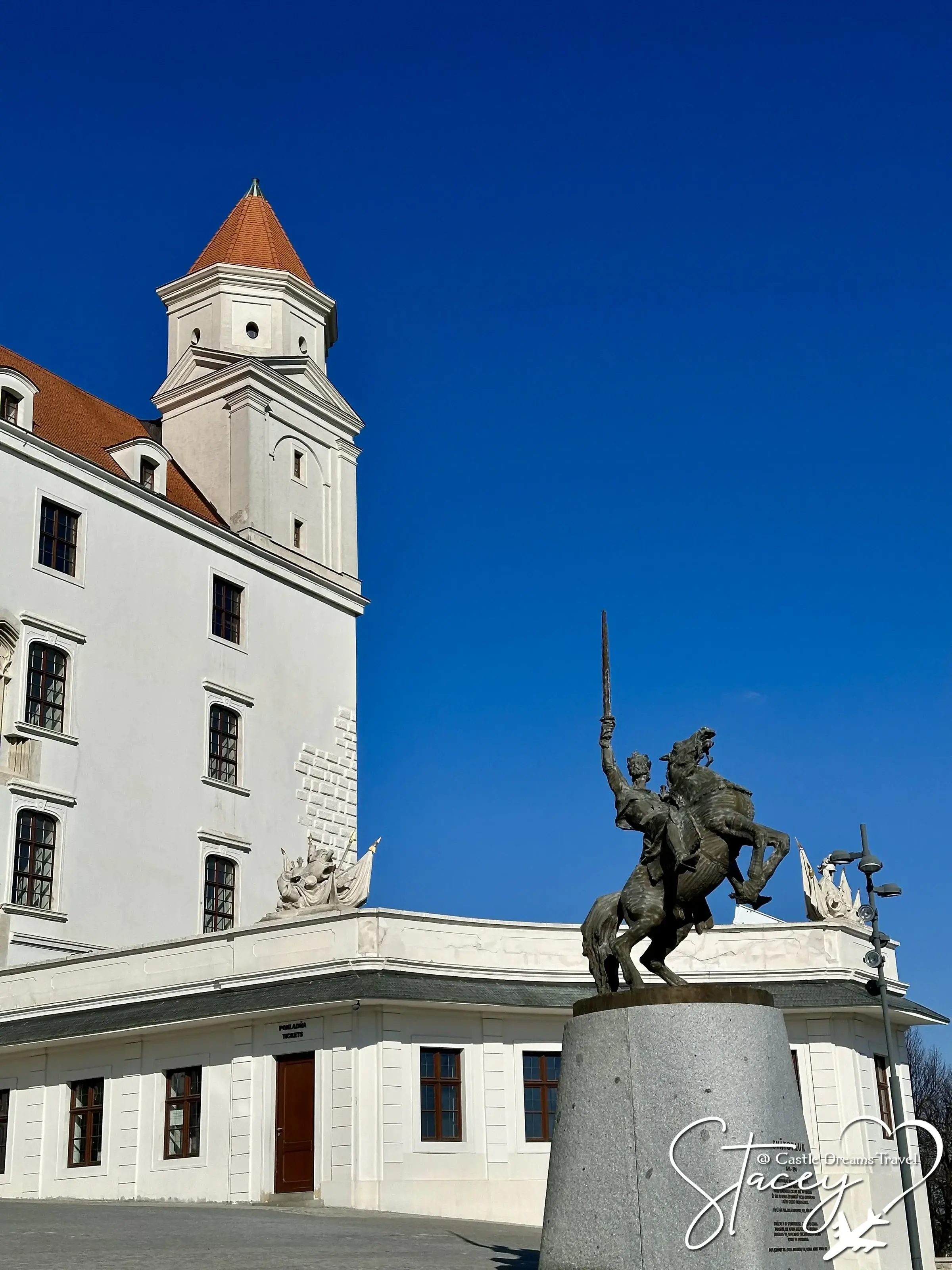 Bratislava Castle's white walls and red roof beside the bronze equestrian statue of Svätopluk